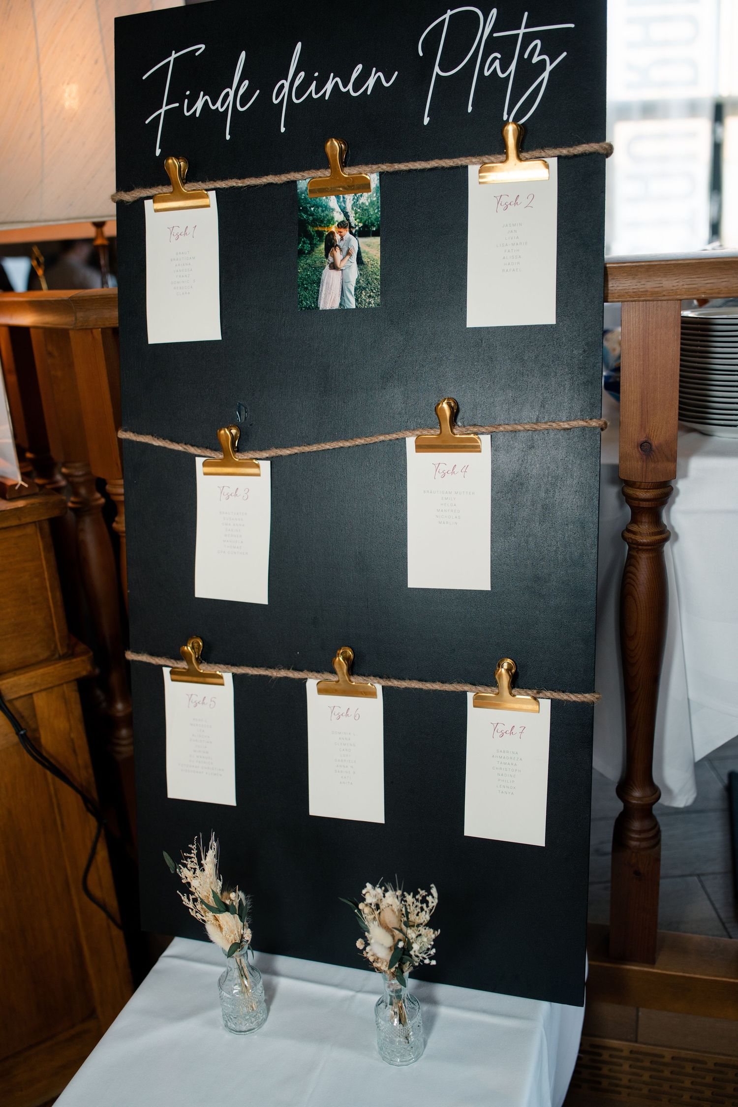 Wedding seating chart on black chalkboard with hanging paper cards and twine.