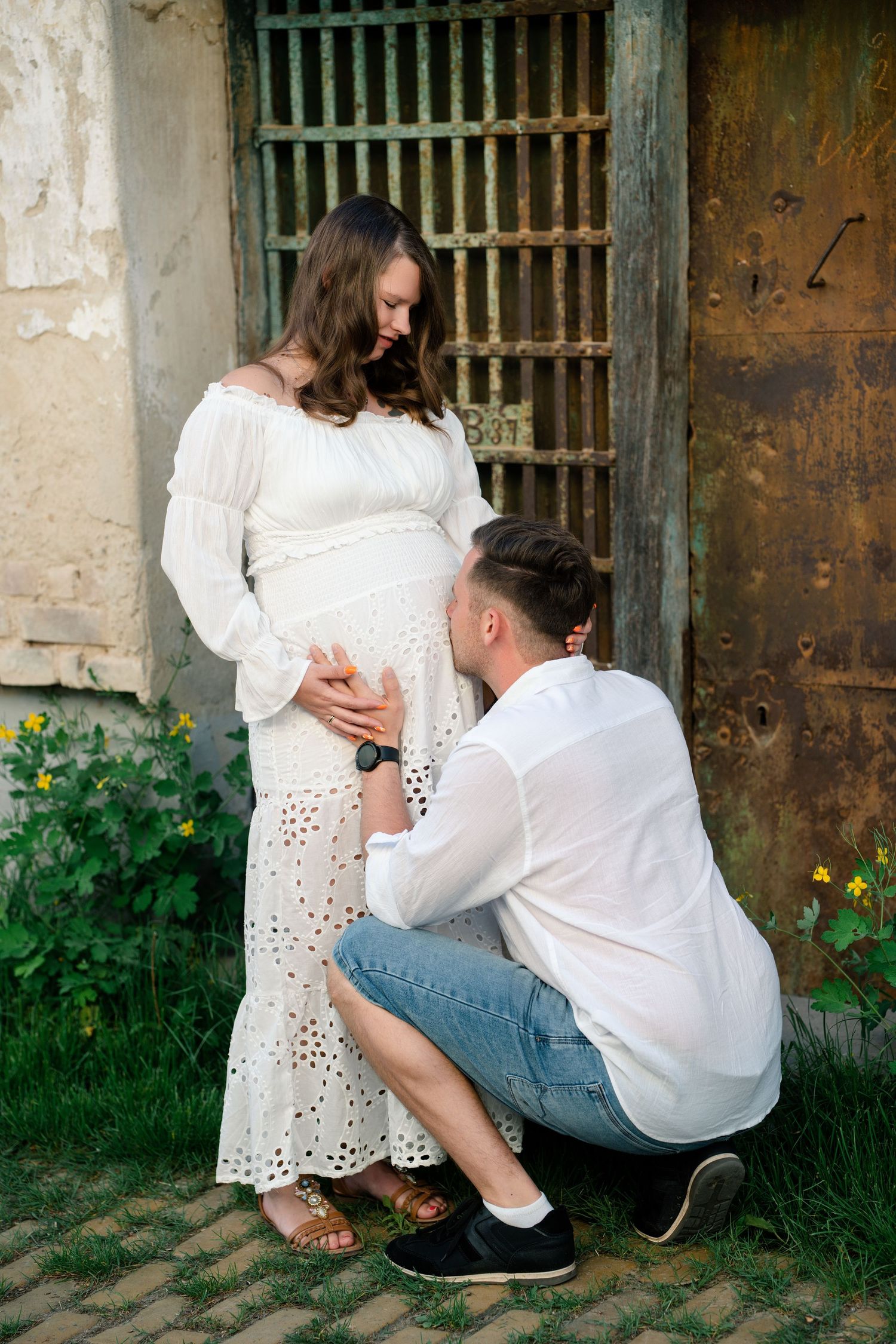 A romantic couple in white outfits poses together near rustic metal doors and greenery in a series of intimate shots.