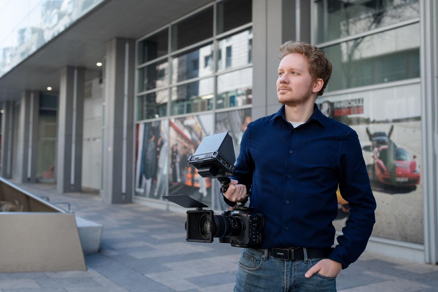 Filmmaker in navy blue sweater operates professional camera equipment while filming on urban street.
