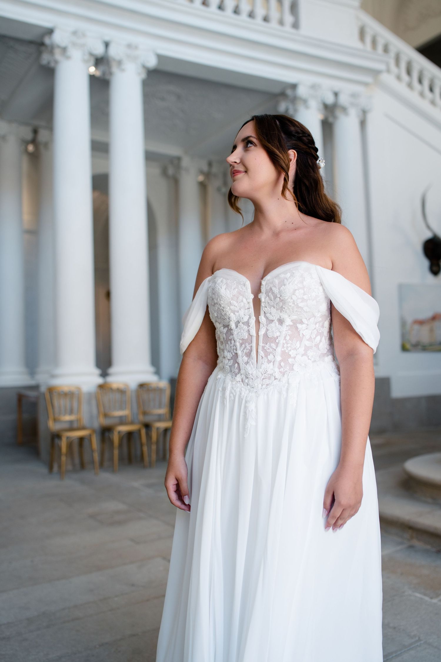 Bride in flowing white dress standing in elegant venue with white columns.