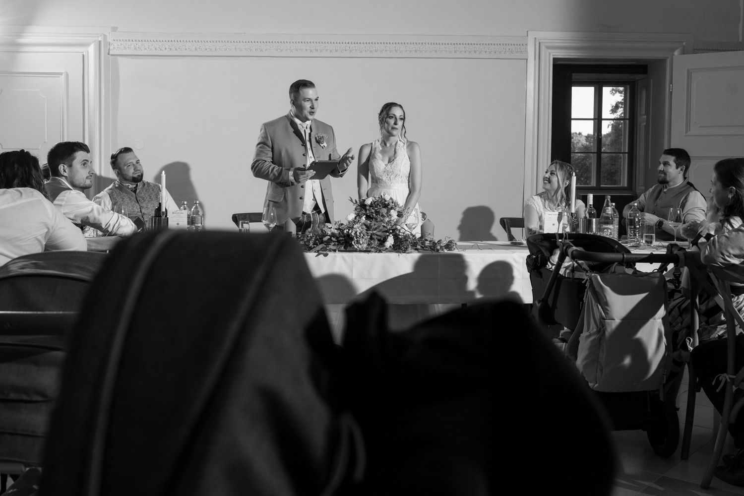 Black and white reception scene with guests gathered at tables.