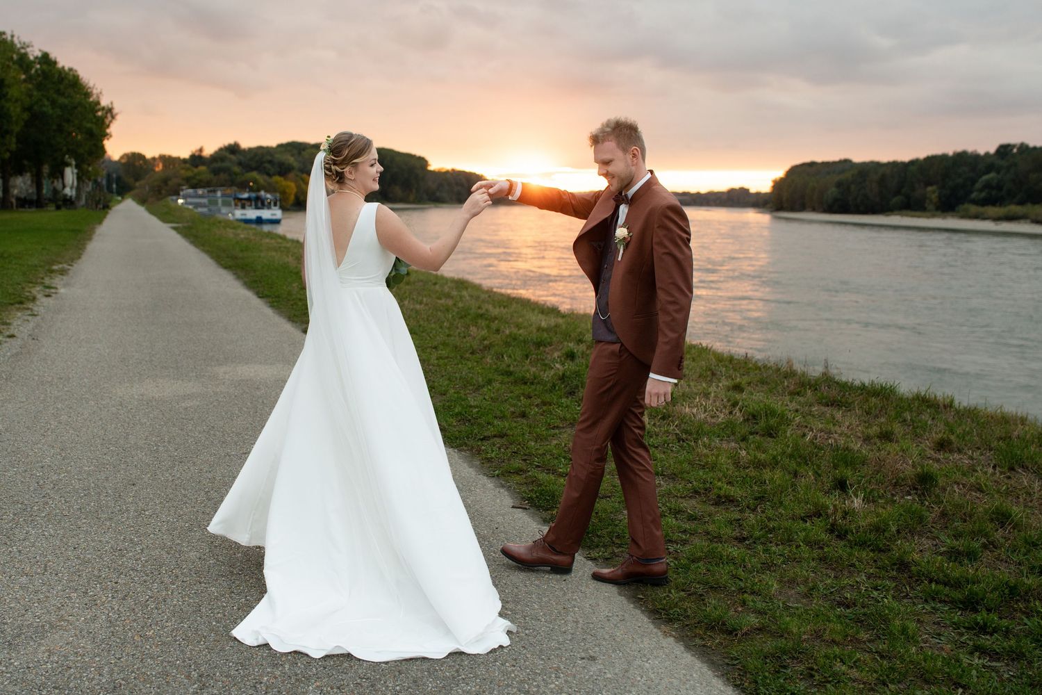 Wedding couple walks along waterfront path during golden sunset.