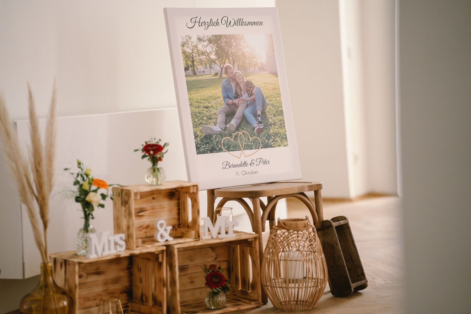 Minimalist wedding decor setup with dried pampas grass, wooden furniture, and soft lighting in a white interior space.