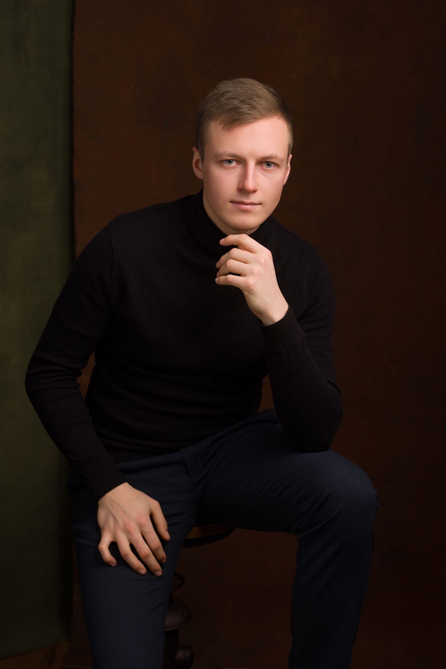 Professional portrait of someone in a black turtleneck sweater seated against a dark background in contemplative pose.
