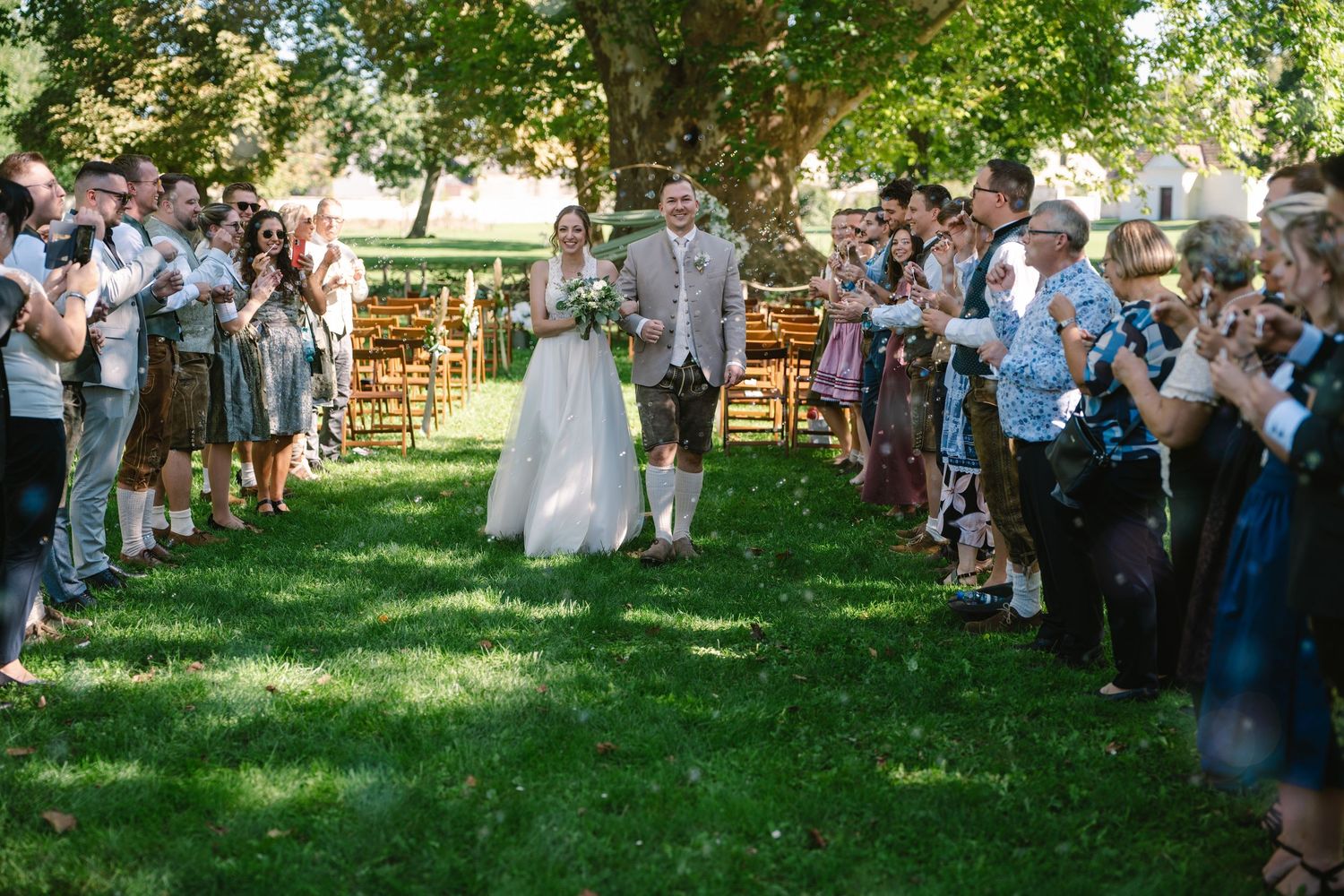 Wedding guests seated on white chairs during an outdoor garden ceremony.