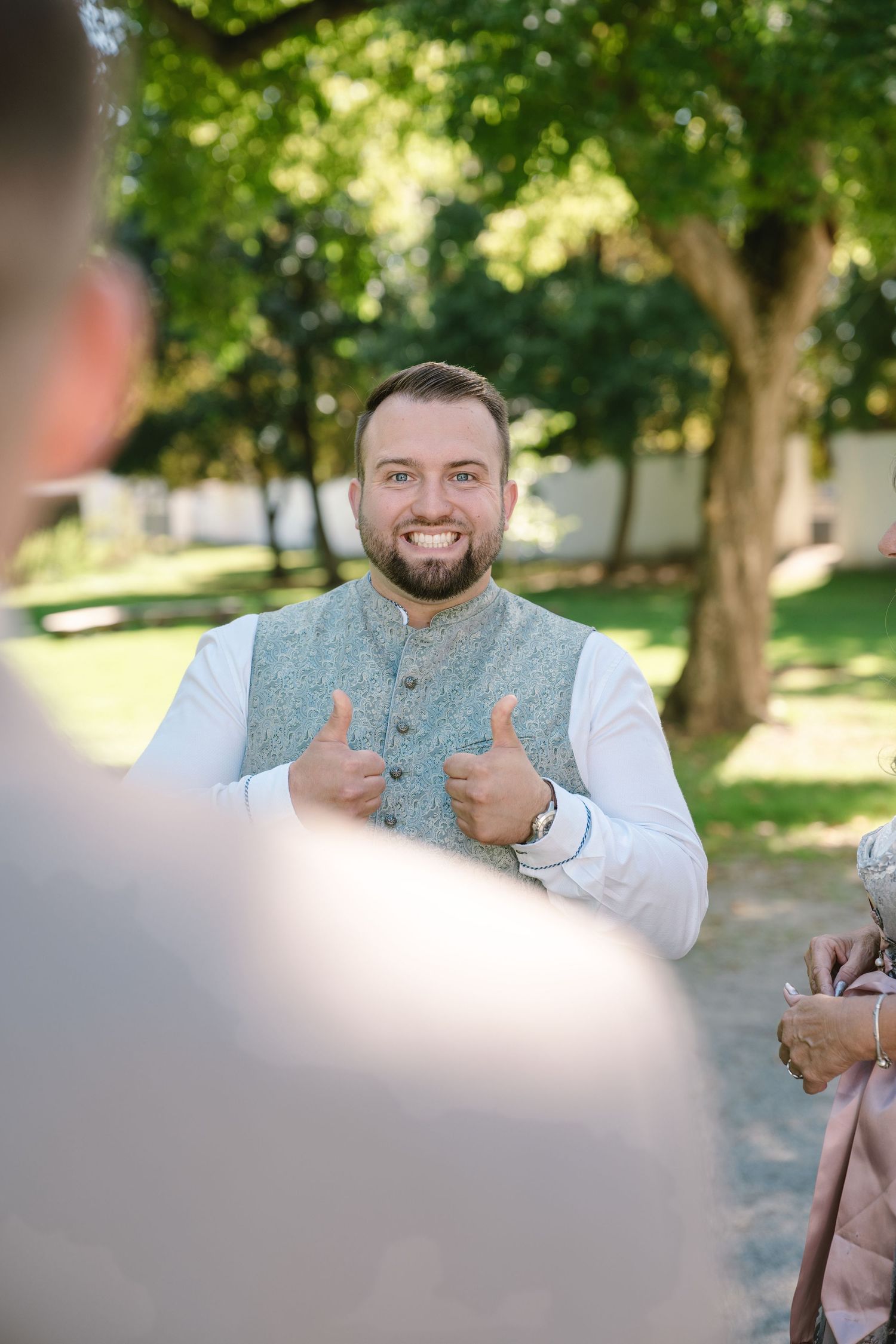 Person in grey vest gives thumbs up gesture outdoors.