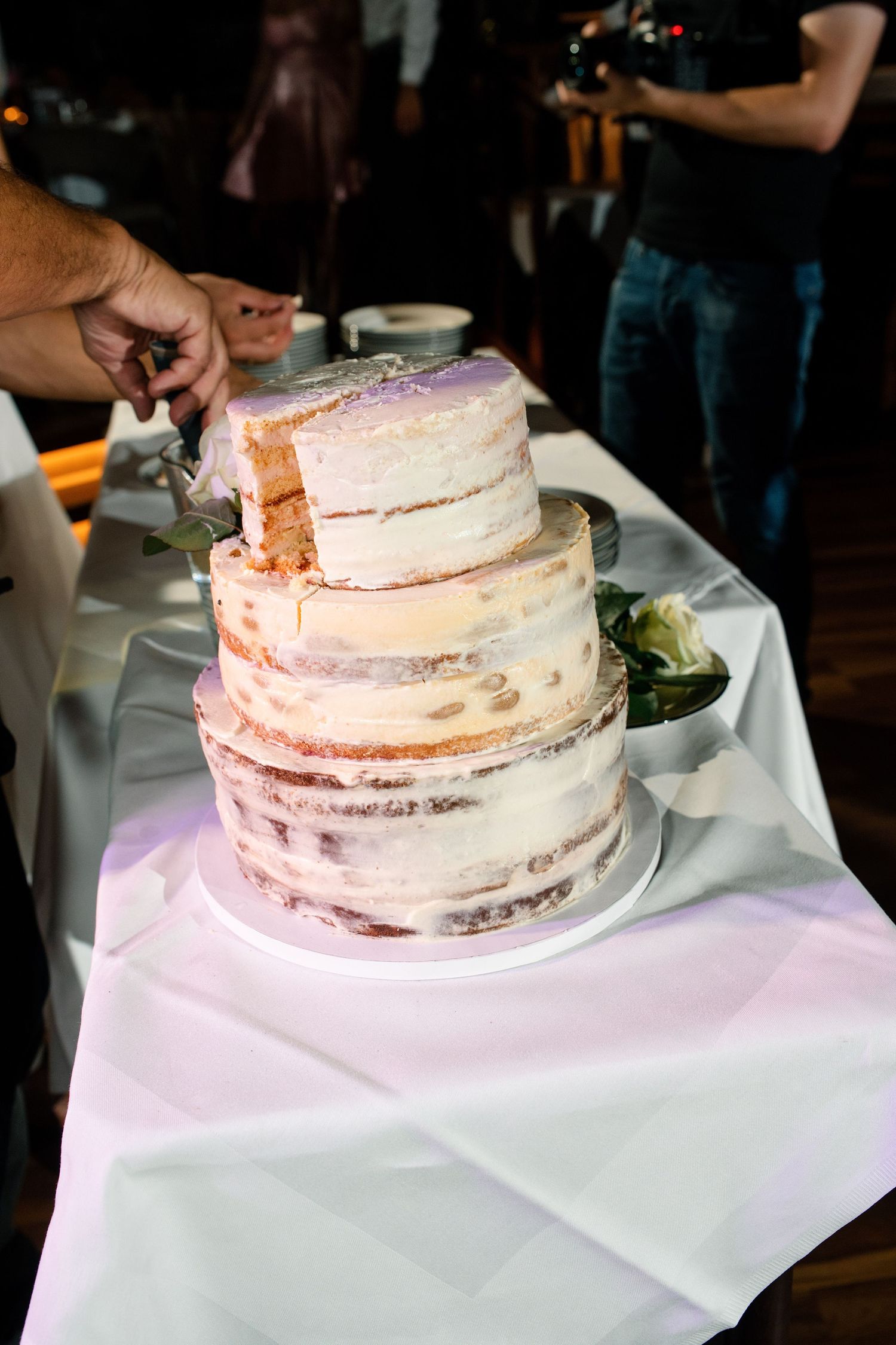 Multi-tiered naked wedding cake with light frosting displayed on white tablecloth.