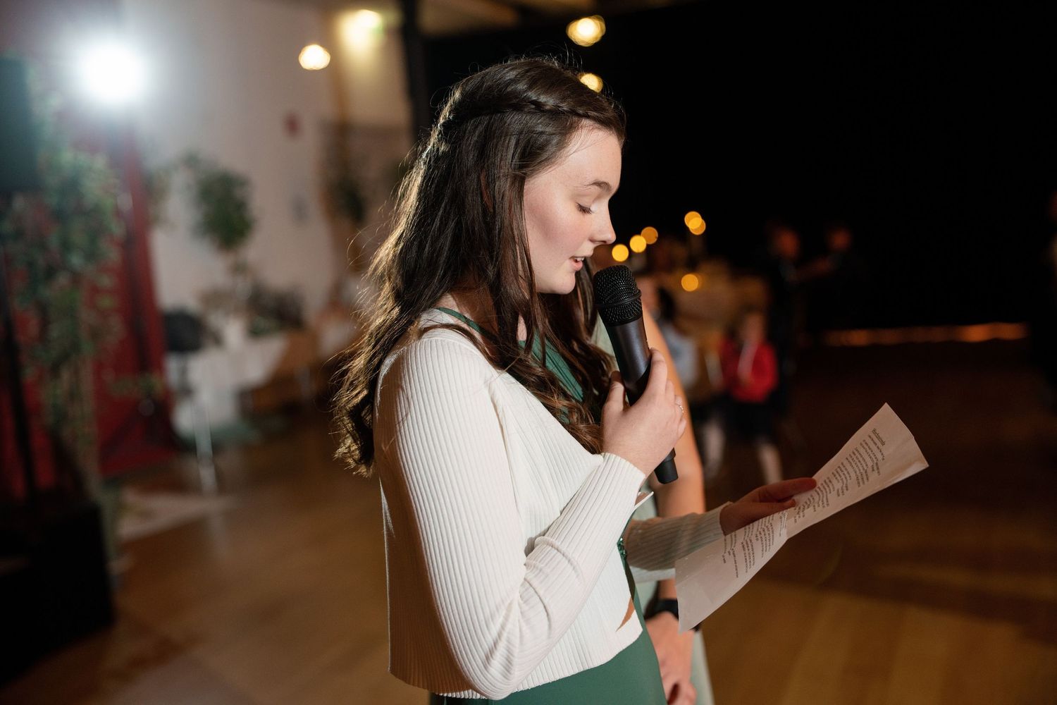 A person reads from a paper in a dimly lit venue during an evening event.
