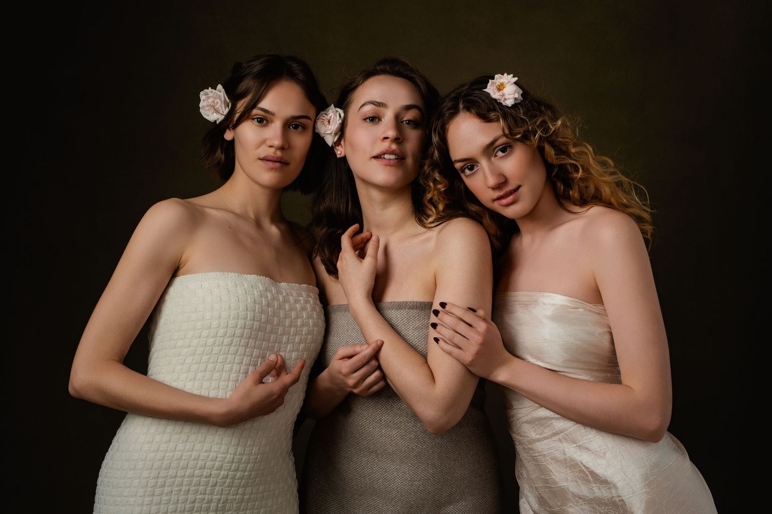 Three people in white strapless dresses pose together in a romantic studio portrait series.