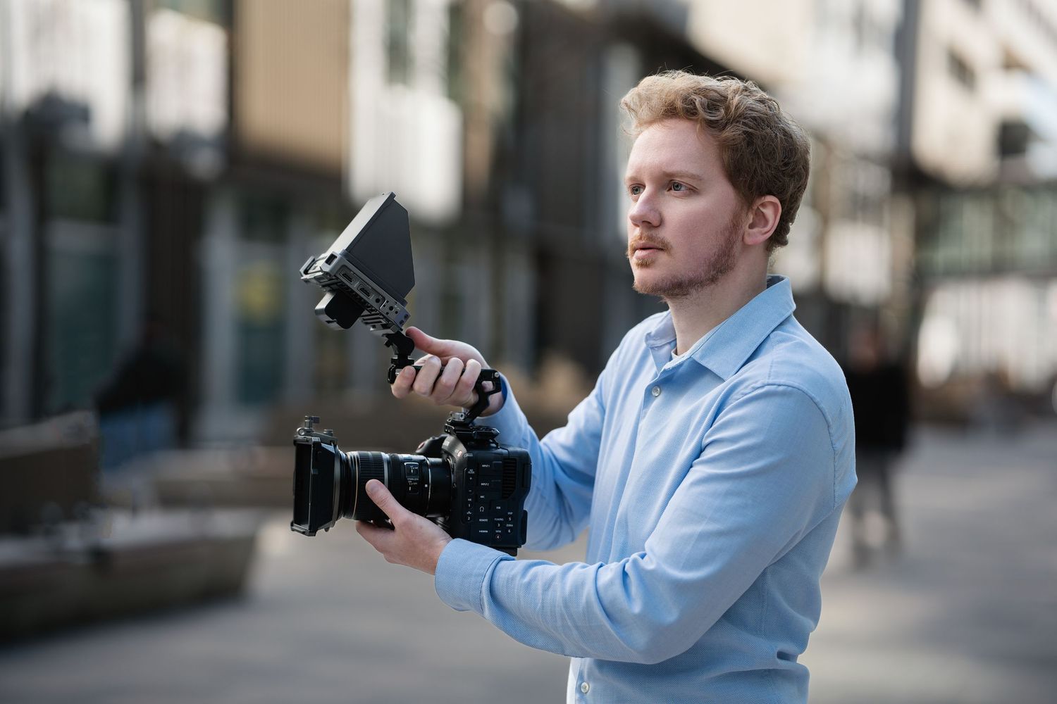Photographer in business casual attire demonstrating different camera angles outdoors.