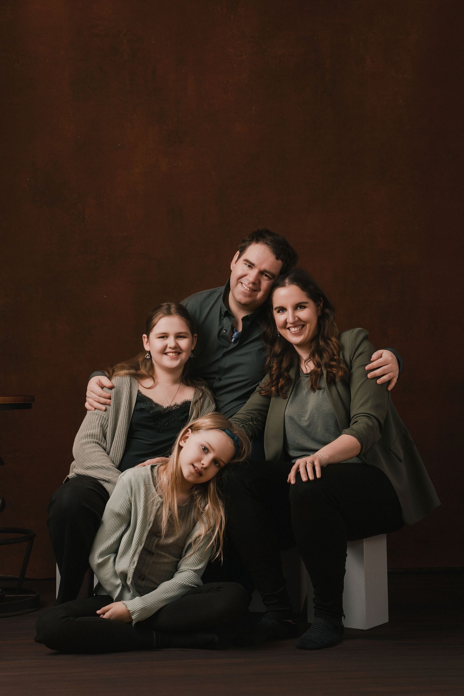 A family poses together against a dark brown backdrop in a series of candid studio portraits.