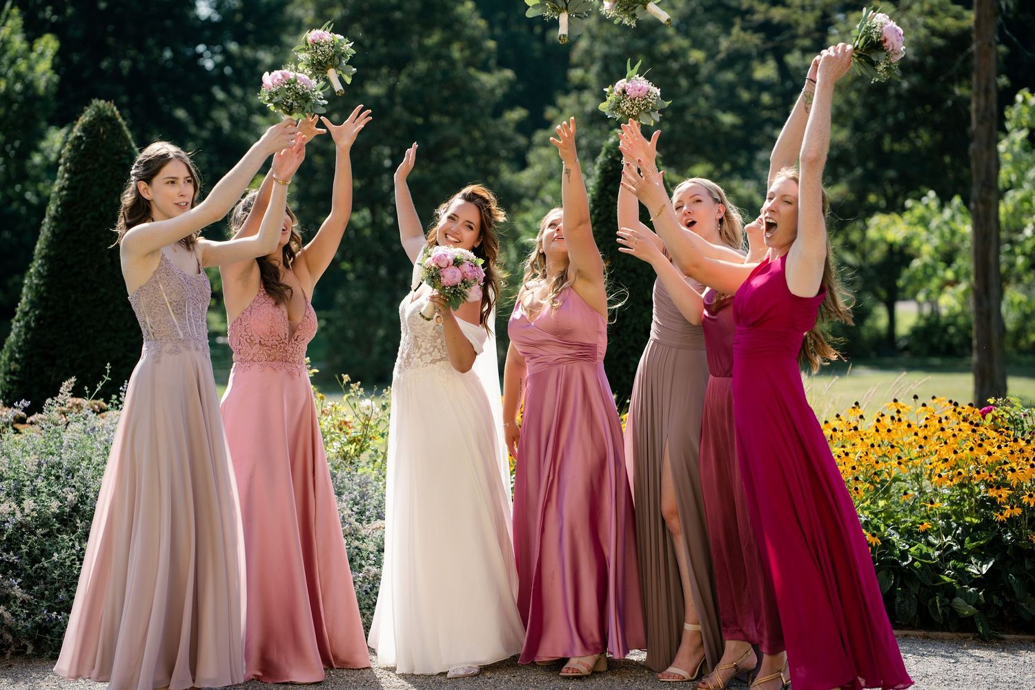 Bridal party wearing ombre pink dresses celebrates in a sunny garden setting.
