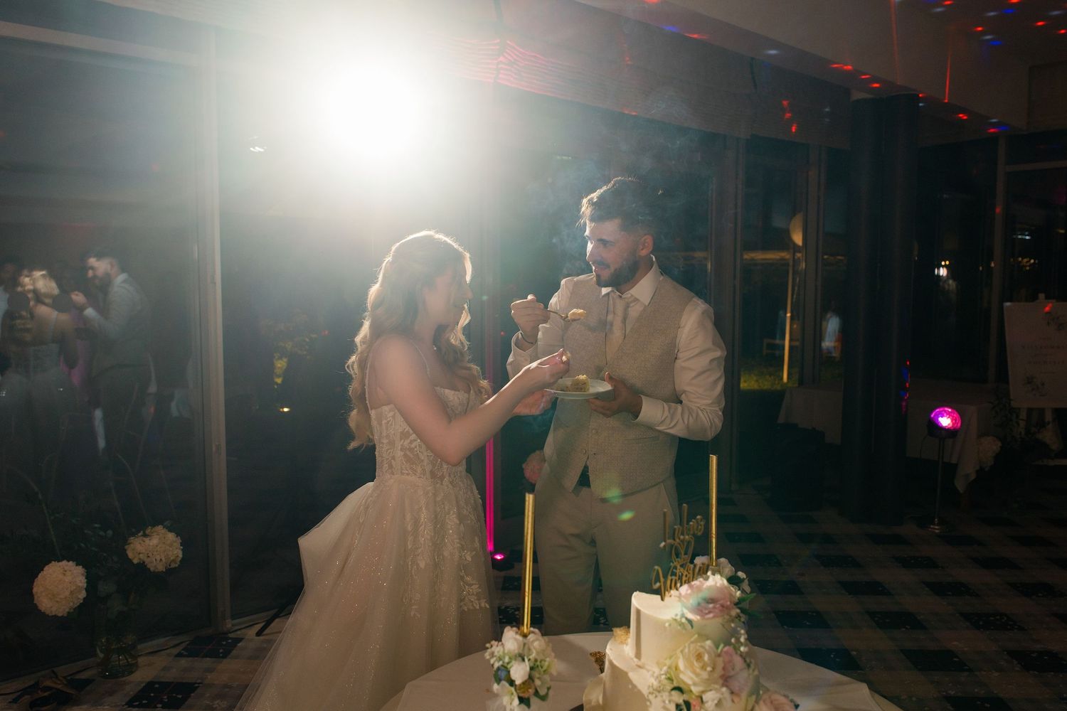 Bride and groom cutting their wedding cake together under warm spotlight at elegant evening reception.