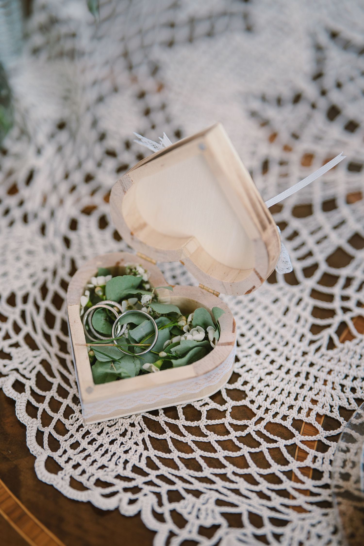 Wedding rings nestled in a small wooden box on delicate white lace doily.