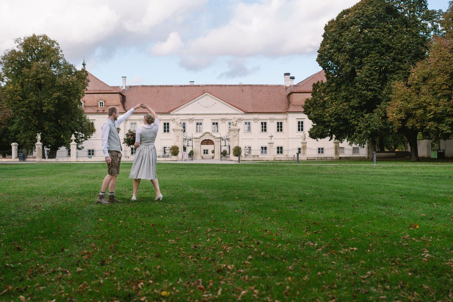 A panoramic view of a grand historic building with manicured lawns and trees on a sunny day.