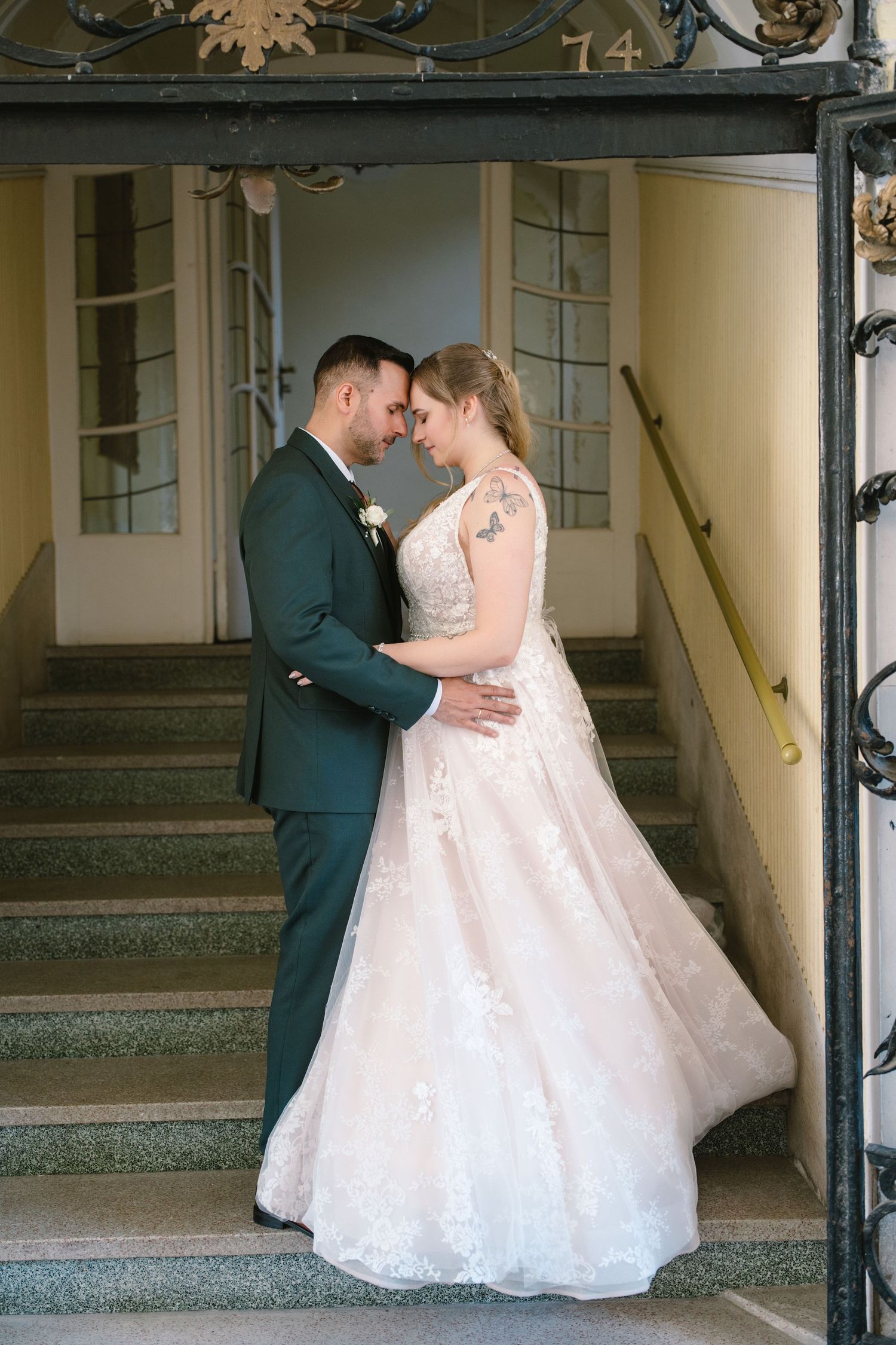 Wedding couple poses on vintage staircase with ornate iron railing.