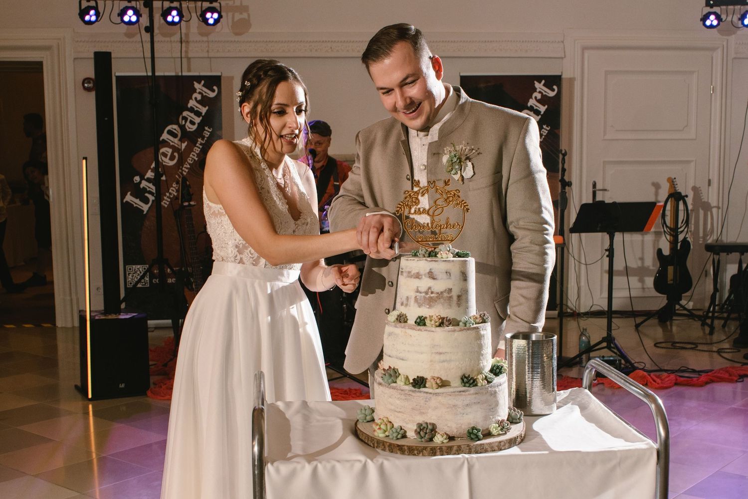 Couple cuts their elegant white wedding cake together during reception celebration.
