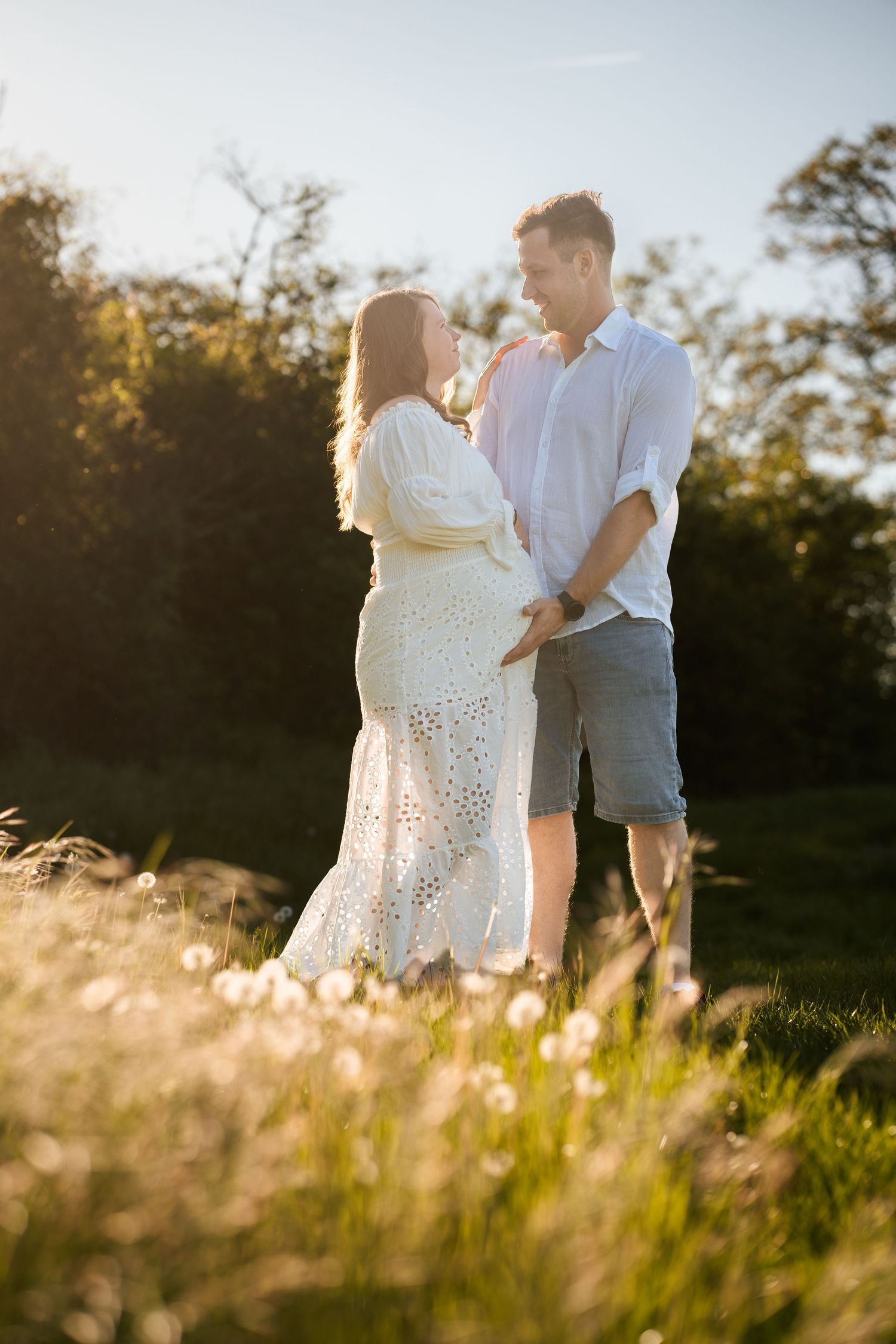 A couple shares tender moments in a sunlit meadow with tall grass during golden hour.