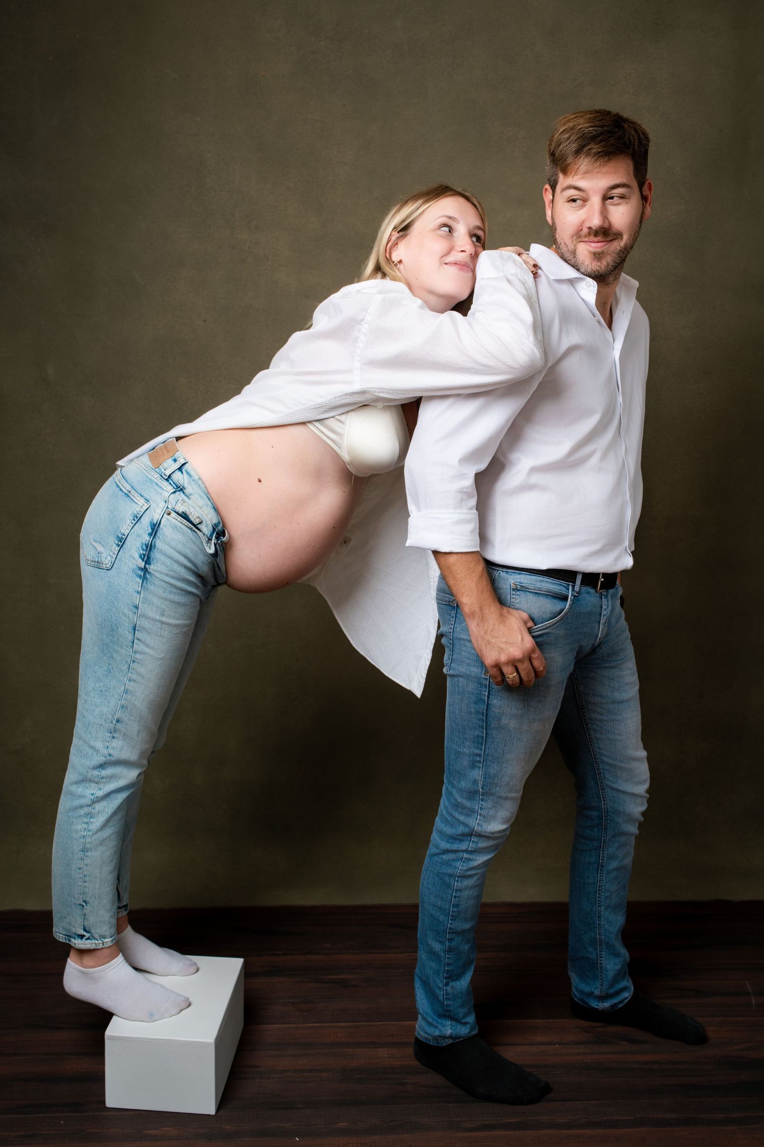 Artistic maternity photos showing creative poses with white cube props against dark studio background.