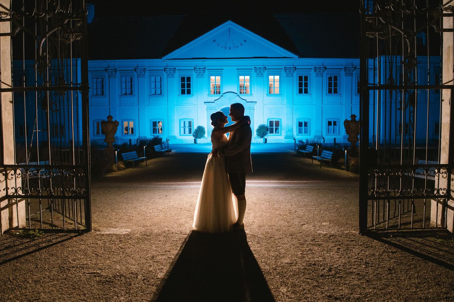 Historic mansion illuminated in blue lighting at night with ornate iron gates.