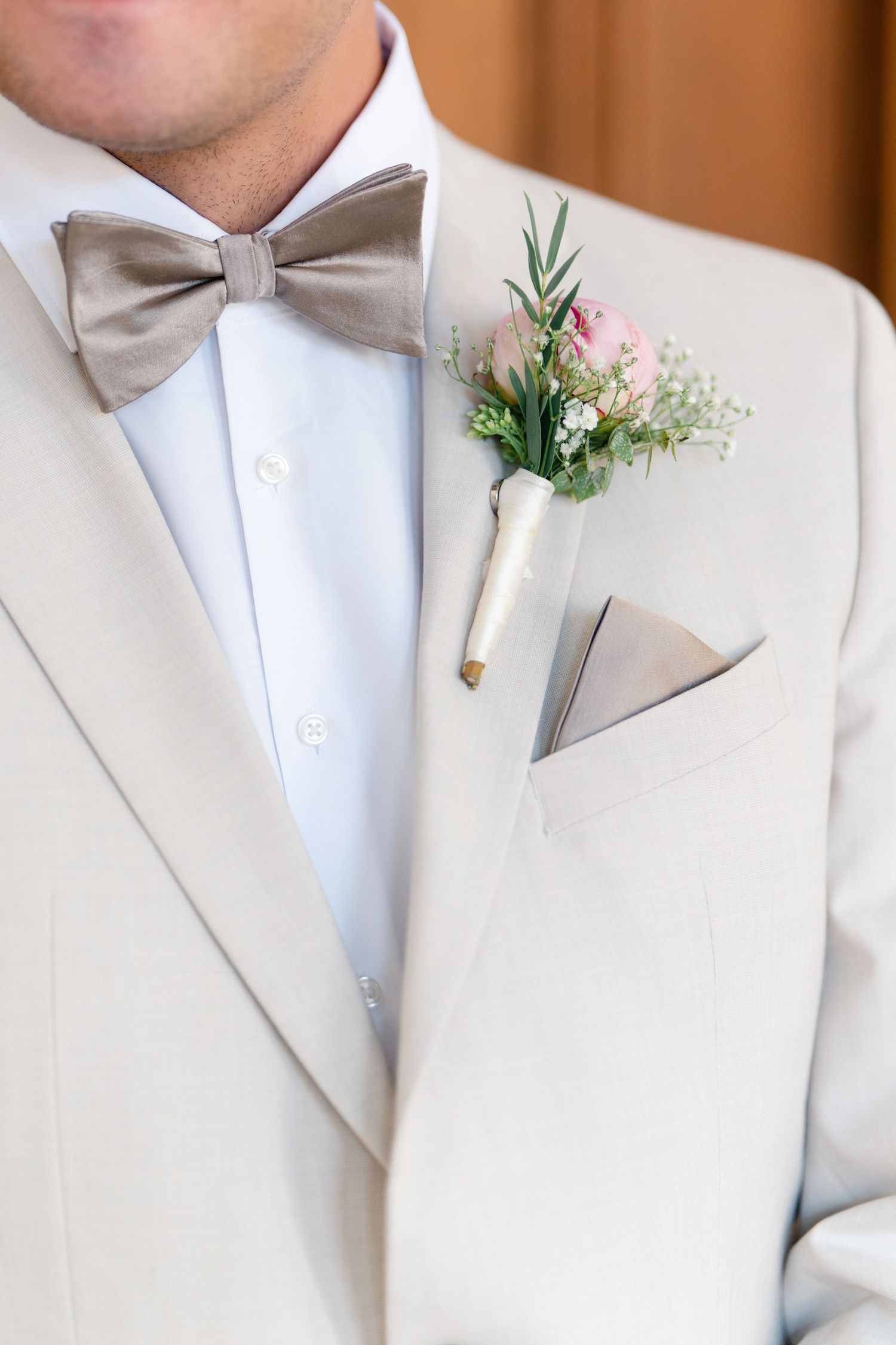 Close-up of white boutonniere with greenery pinned to a light colored suit lapel.