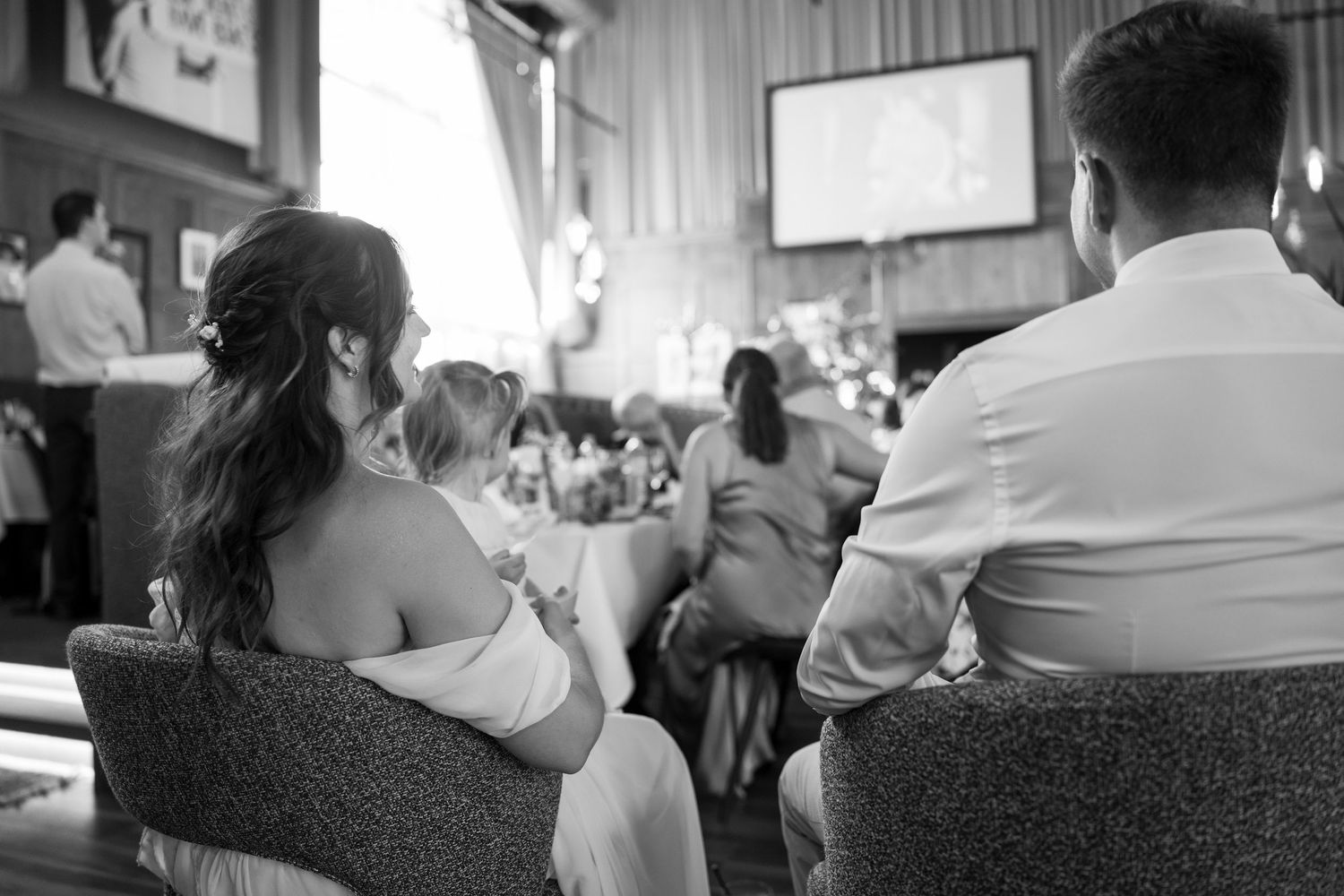 Wedding guests seated at reception tables in soft natural lighting.