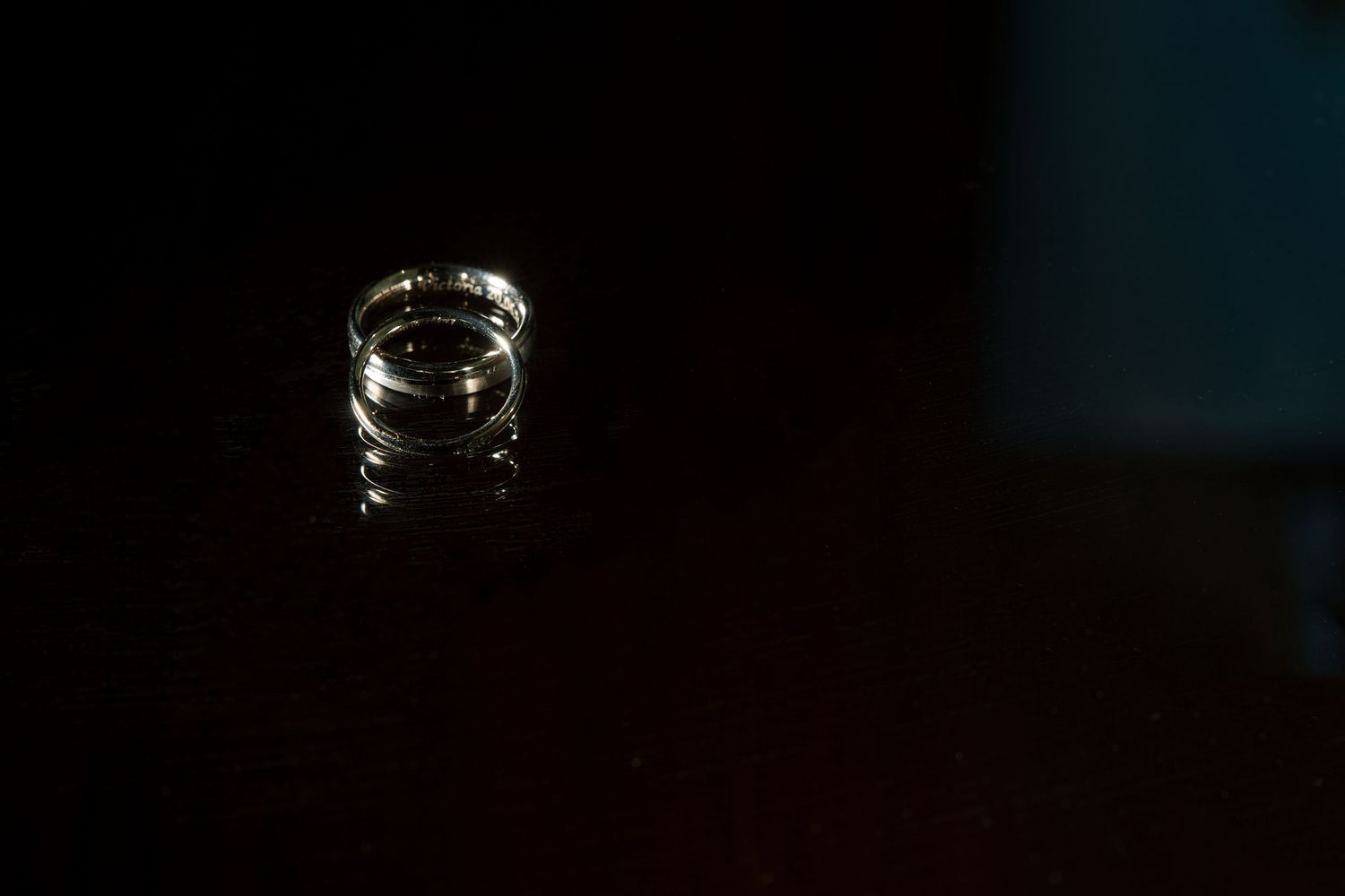 Two gold wedding rings resting on a dark reflective surface in dramatic low-key lighting.