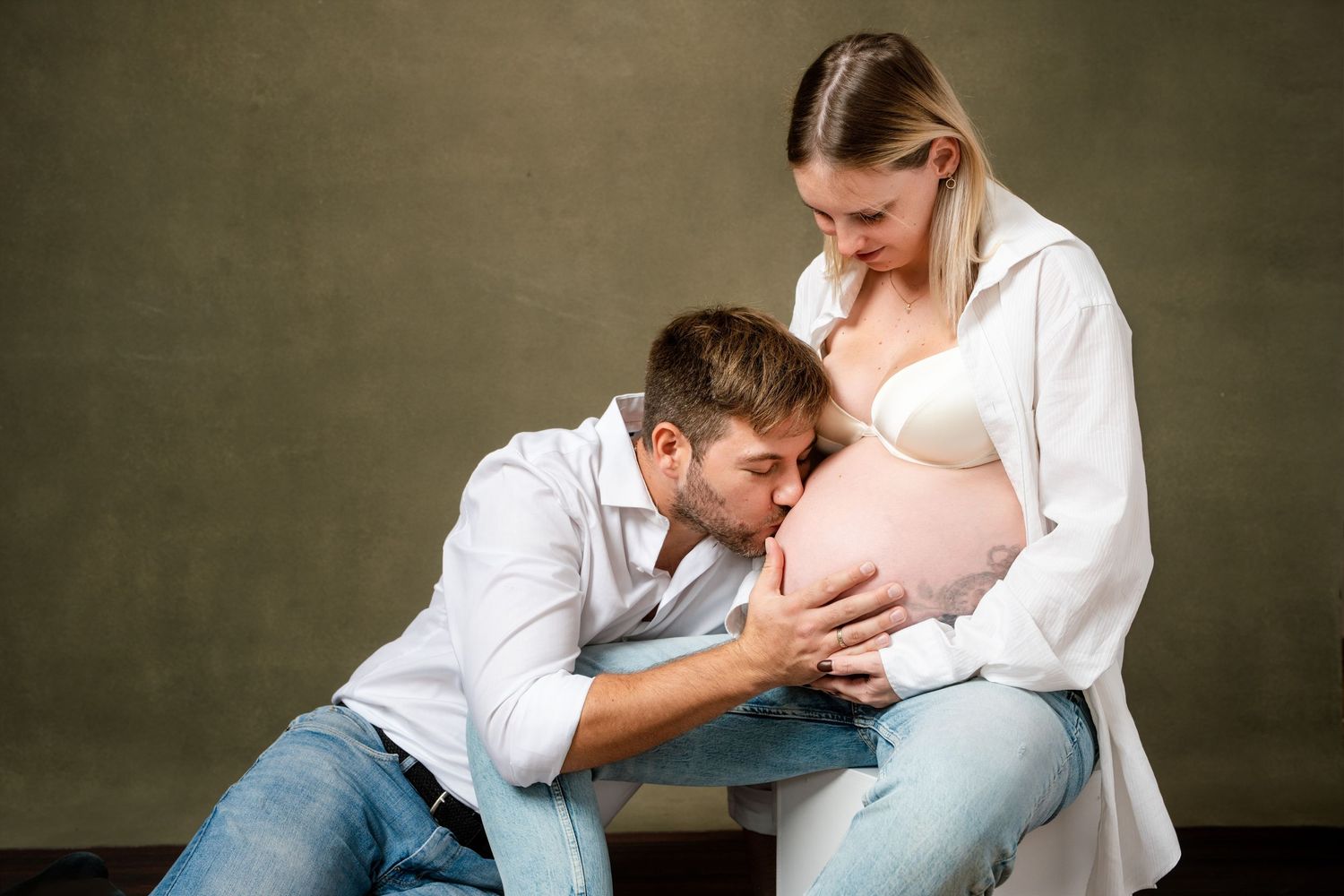 Loving family photography session with coordinated white tops and denim in studio setting.