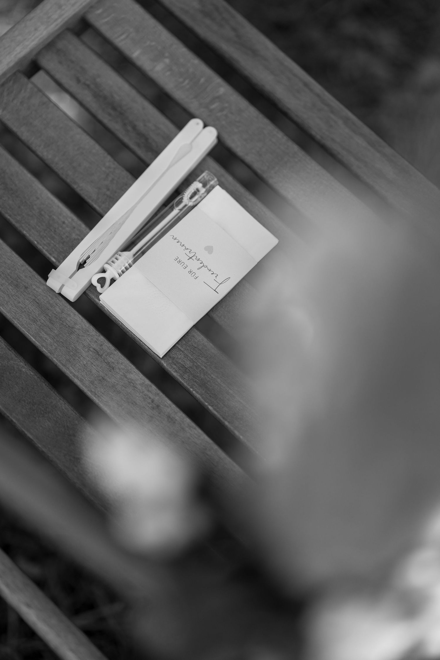 Black and white detail shot of wedding invitation on wooden bench.