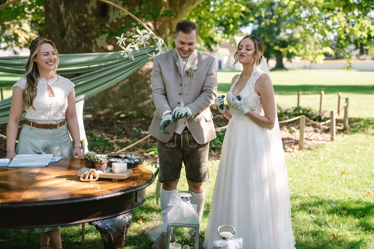 Outdoor wedding reception with decorated tables under green trees.