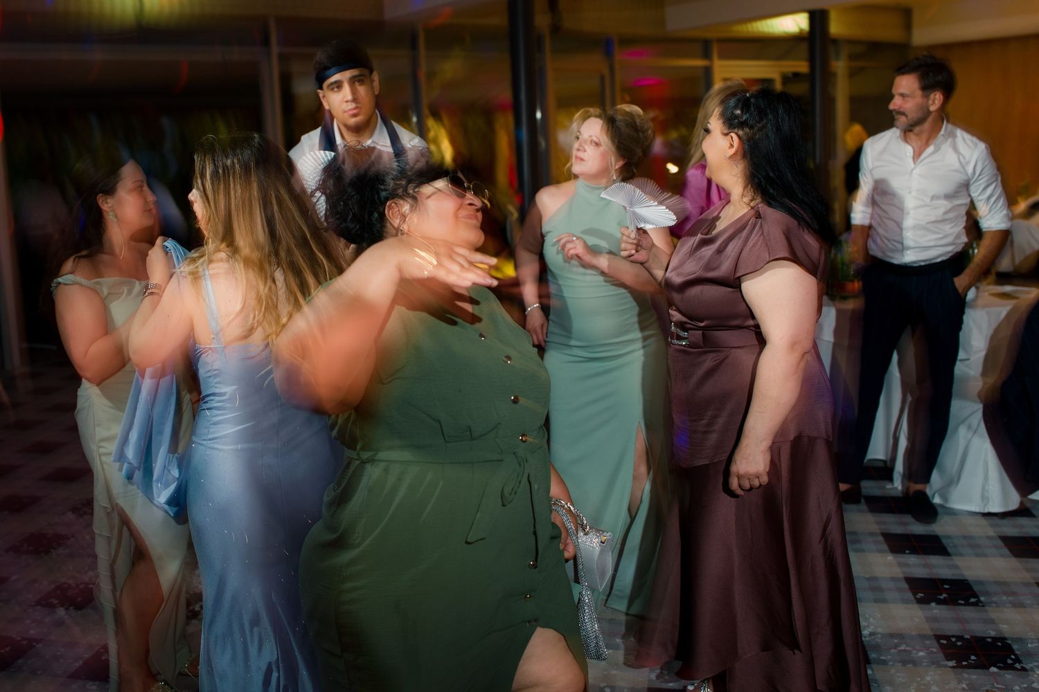 Guests dancing joyfully at a wedding reception in formal attire, including green and purple dresses.
