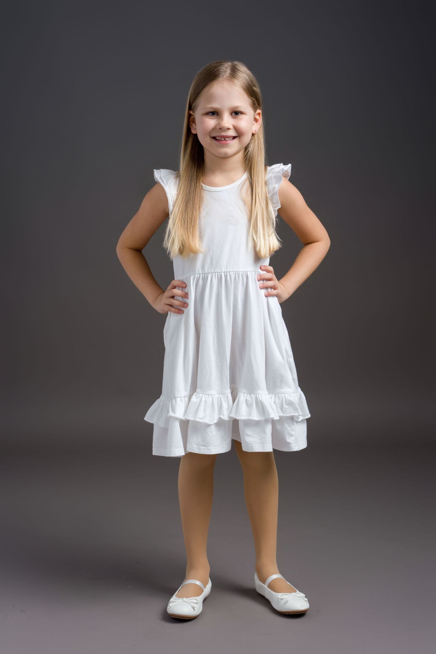 A series of photos showing a child in a white ruffled dress and white shoes against a dark gray background.