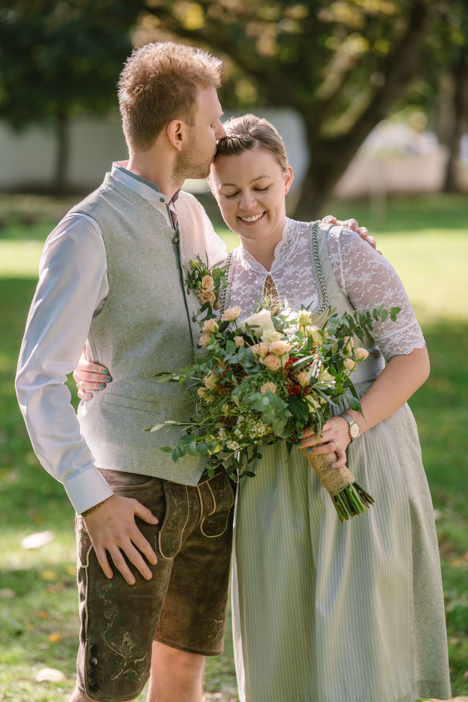 A couple in traditional Bavarian attire share an intimate moment outdoors with autumn flowers and greenery.