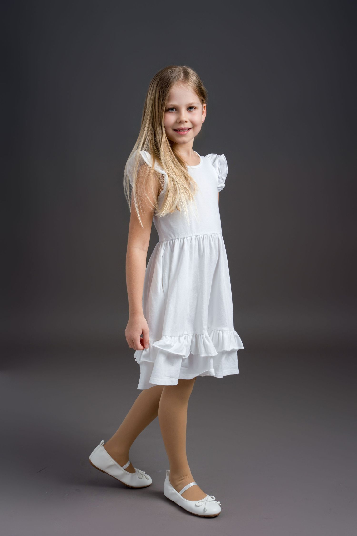 A series of studio photos showing a child in a white summer dress and ballet flats making dynamic poses.