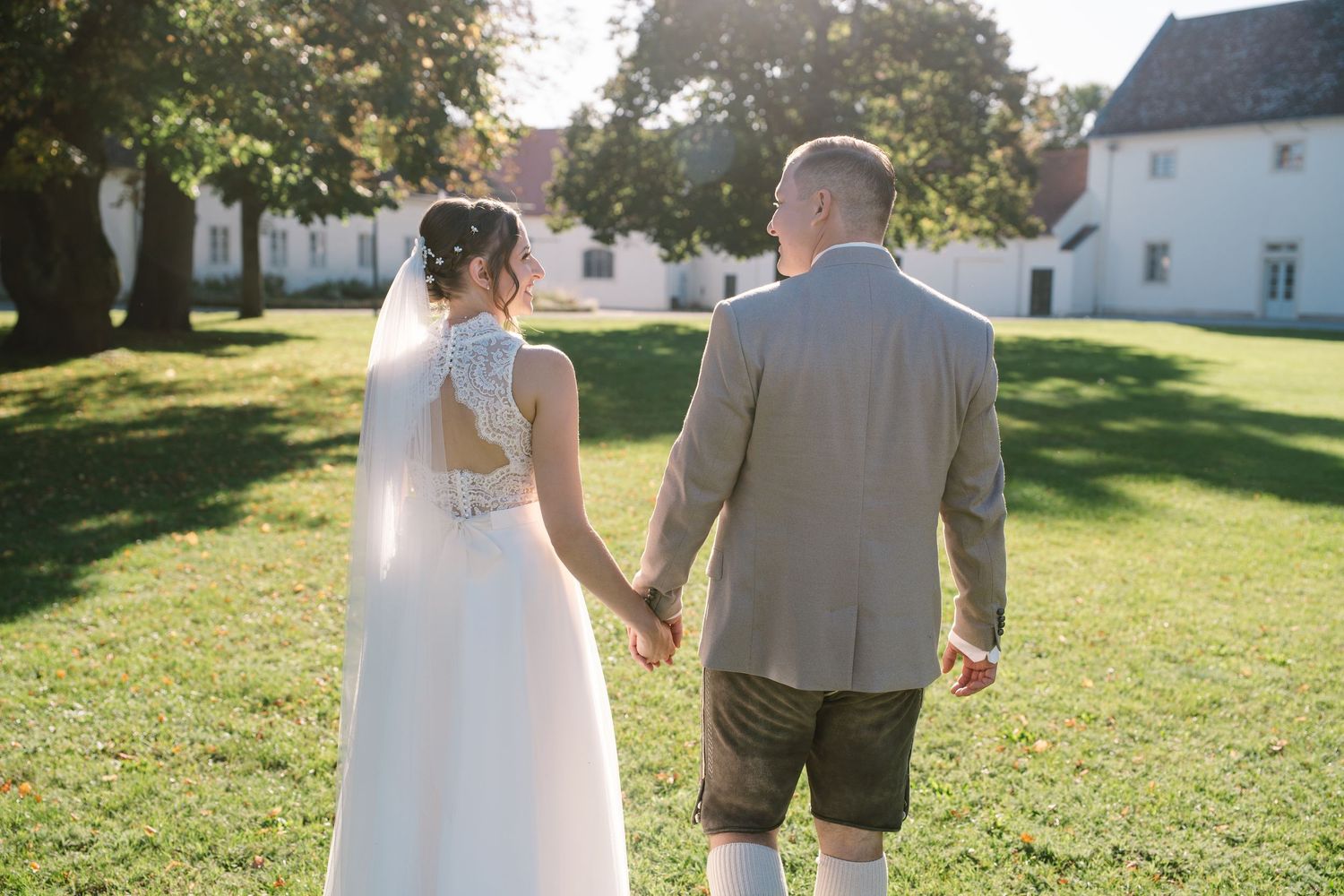 Sun-drenched wedding photos on a sprawling lawn with white buildings in background.