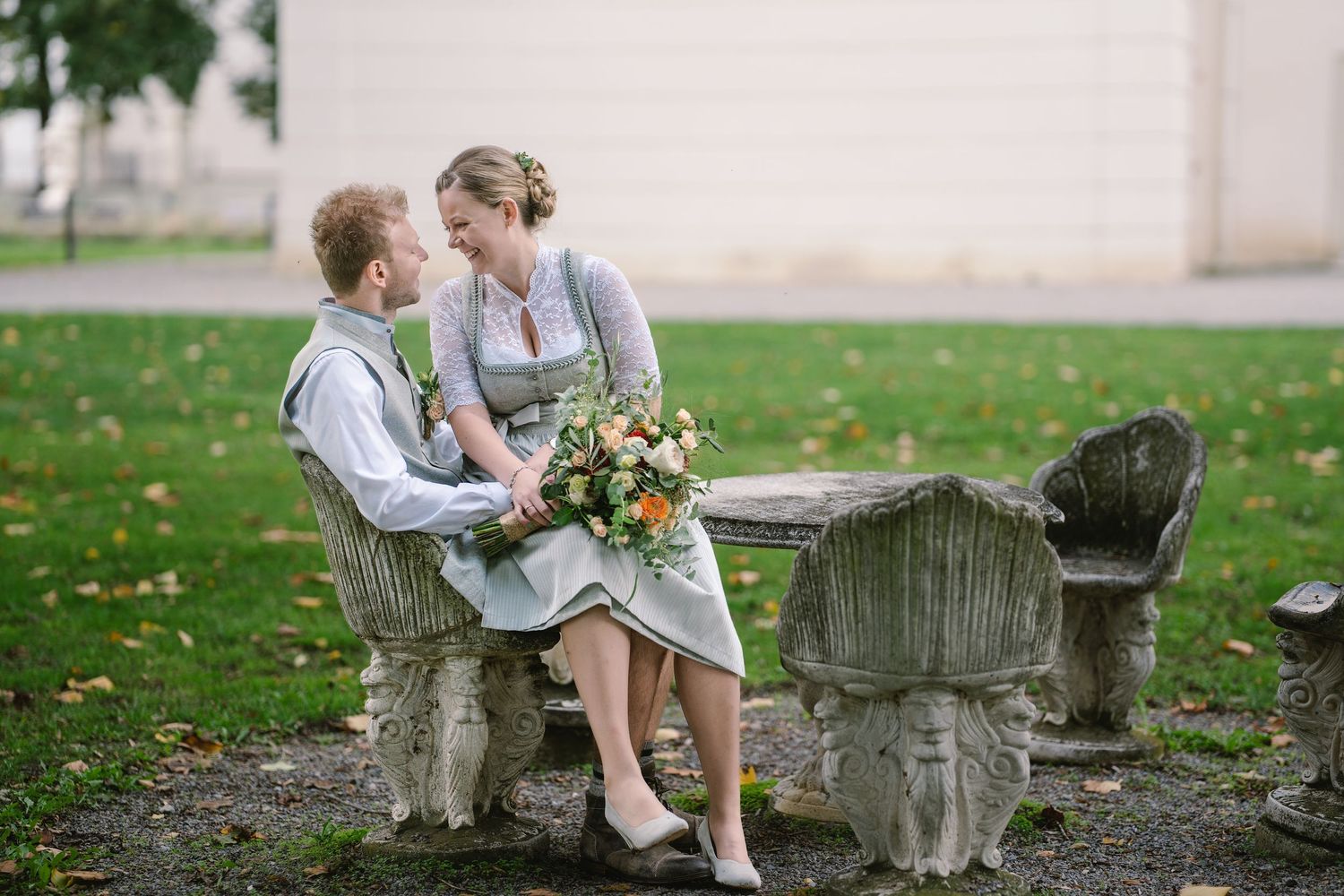 Couple in coordinated sage green and white outfits sitting together on a stone bench in a park.