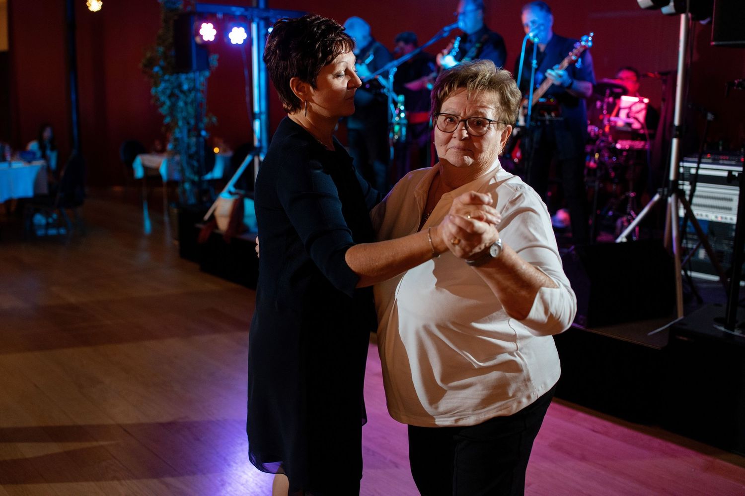 Couples dancing at an indoor reception with colorful lighting and live band in background.