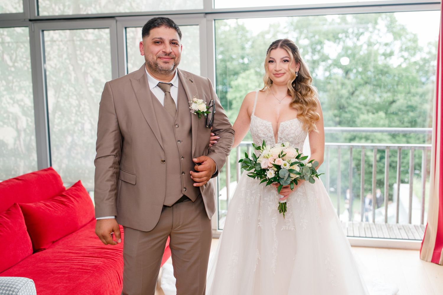 Bride in white gown holding bouquet stands with groom in brown suit at elegant wedding venue.
