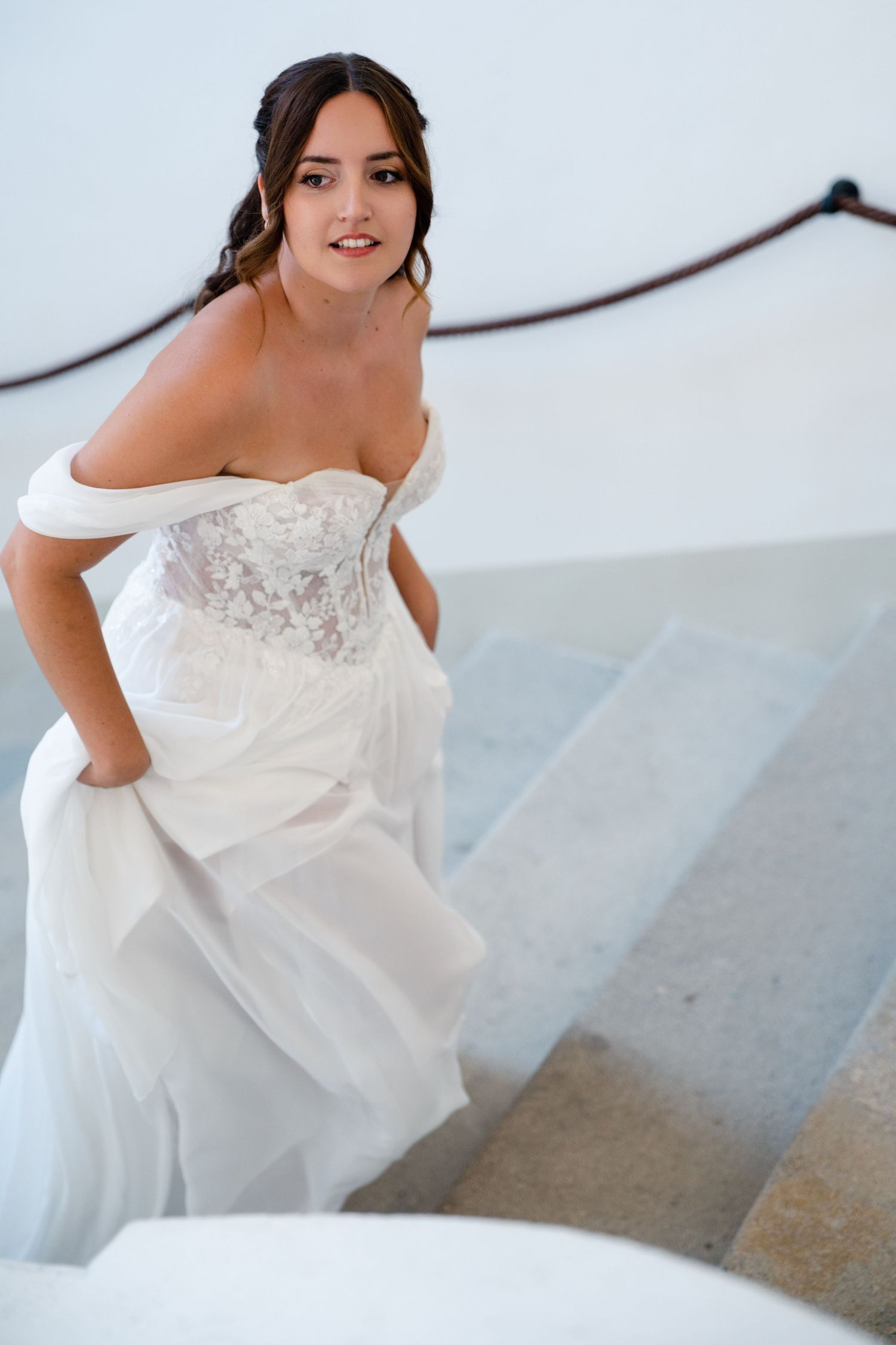 Bride in white gown ascending elegant stairs.