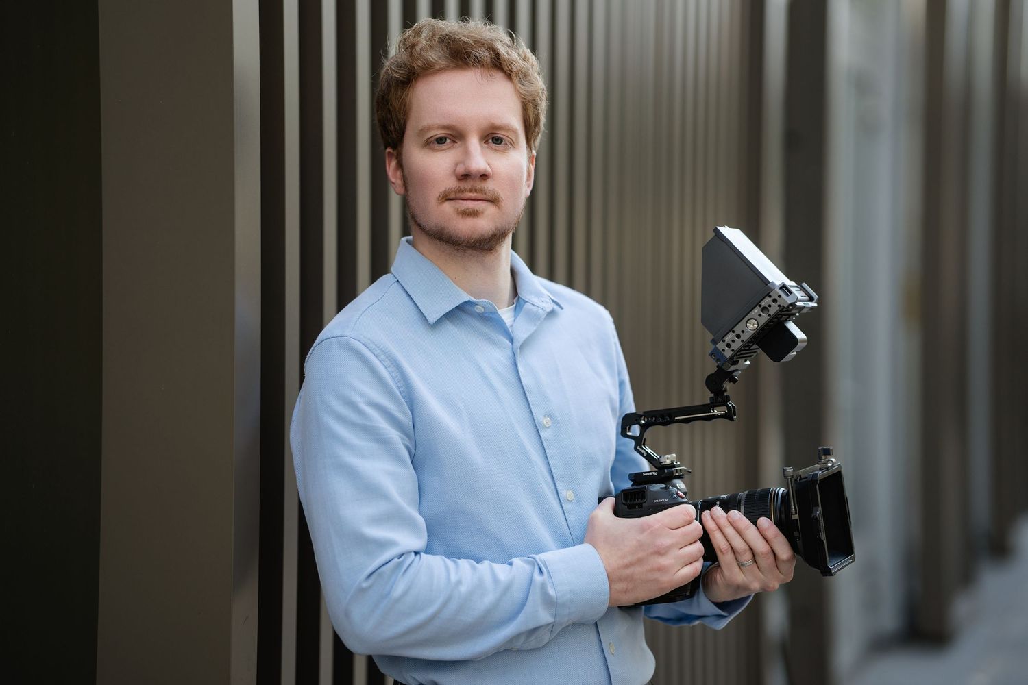 Professional photographer in light blue shirt holding camera equipment indoors.