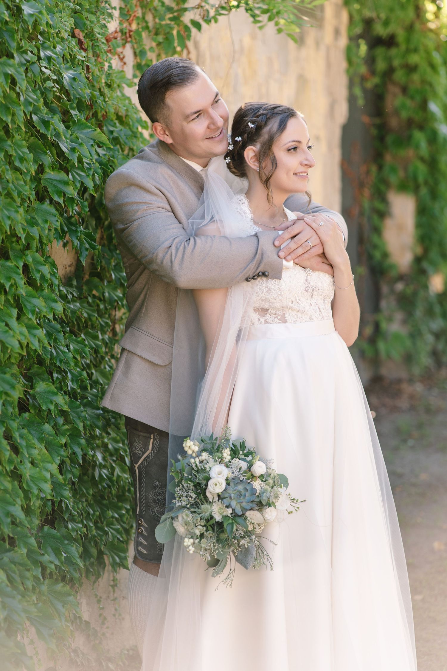 Couple embracing in romantic garden setting with white floral bouquet.