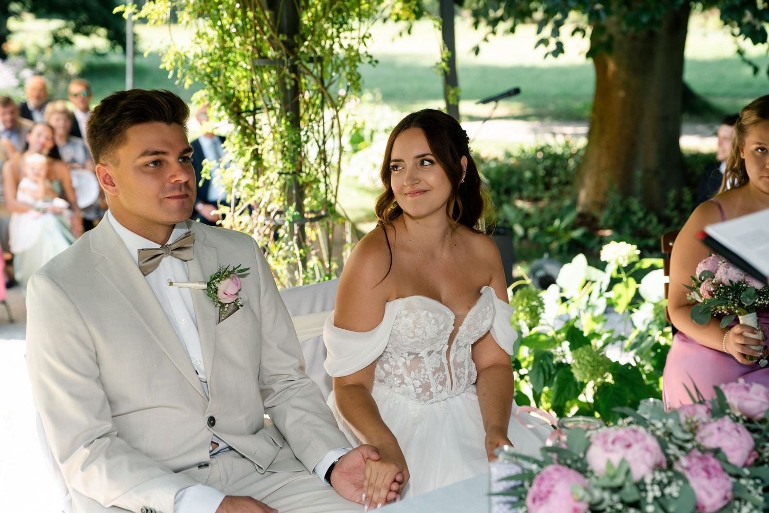 Outdoor wedding ceremony seating under trees with floral decorations.