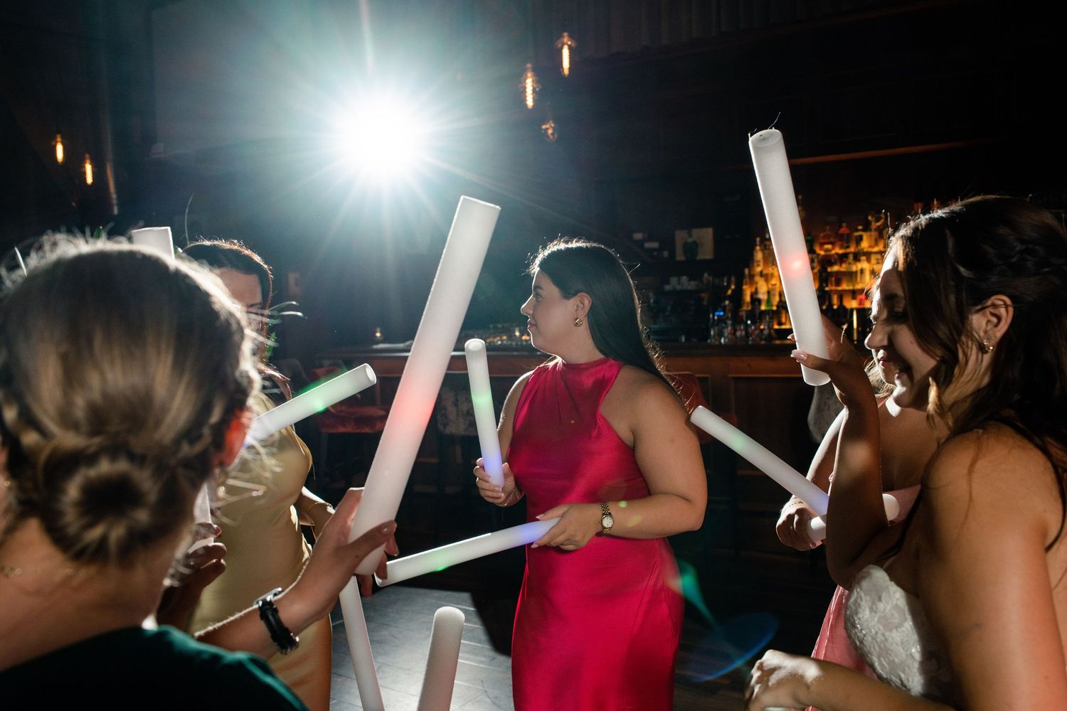 Party guests holding glowing LED foam sticks on a dark dance floor.