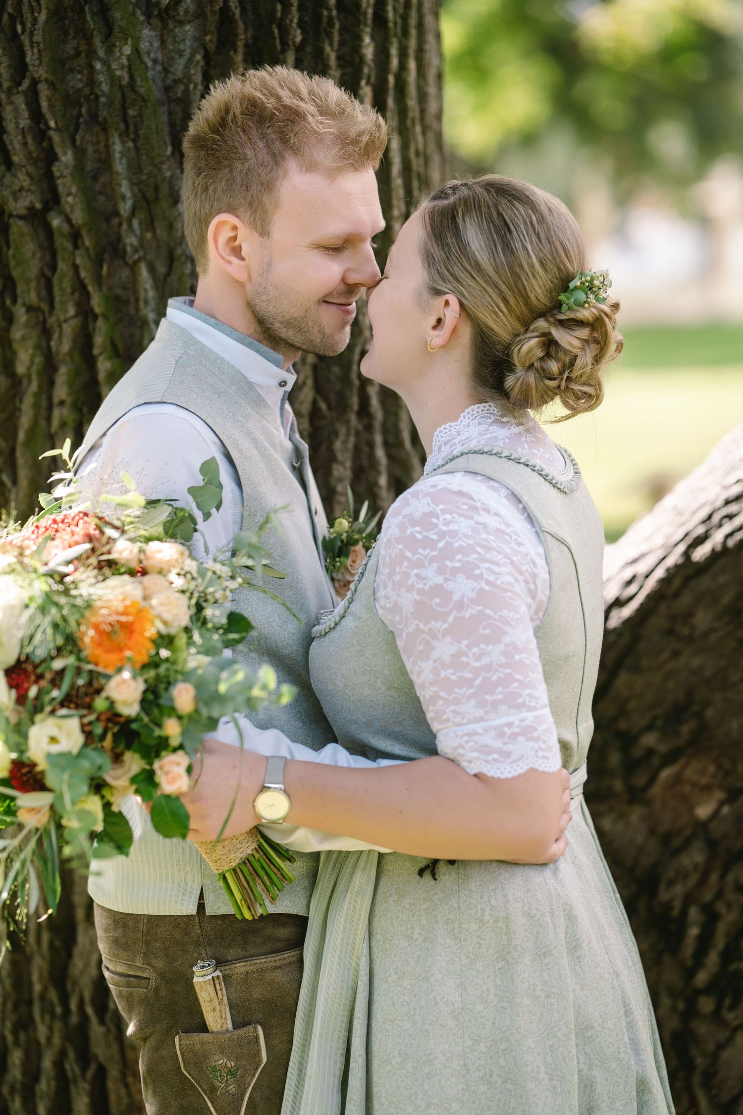 Romantic couple in vintage attire sharing tender moments against a tree trunk in a garden setting.
