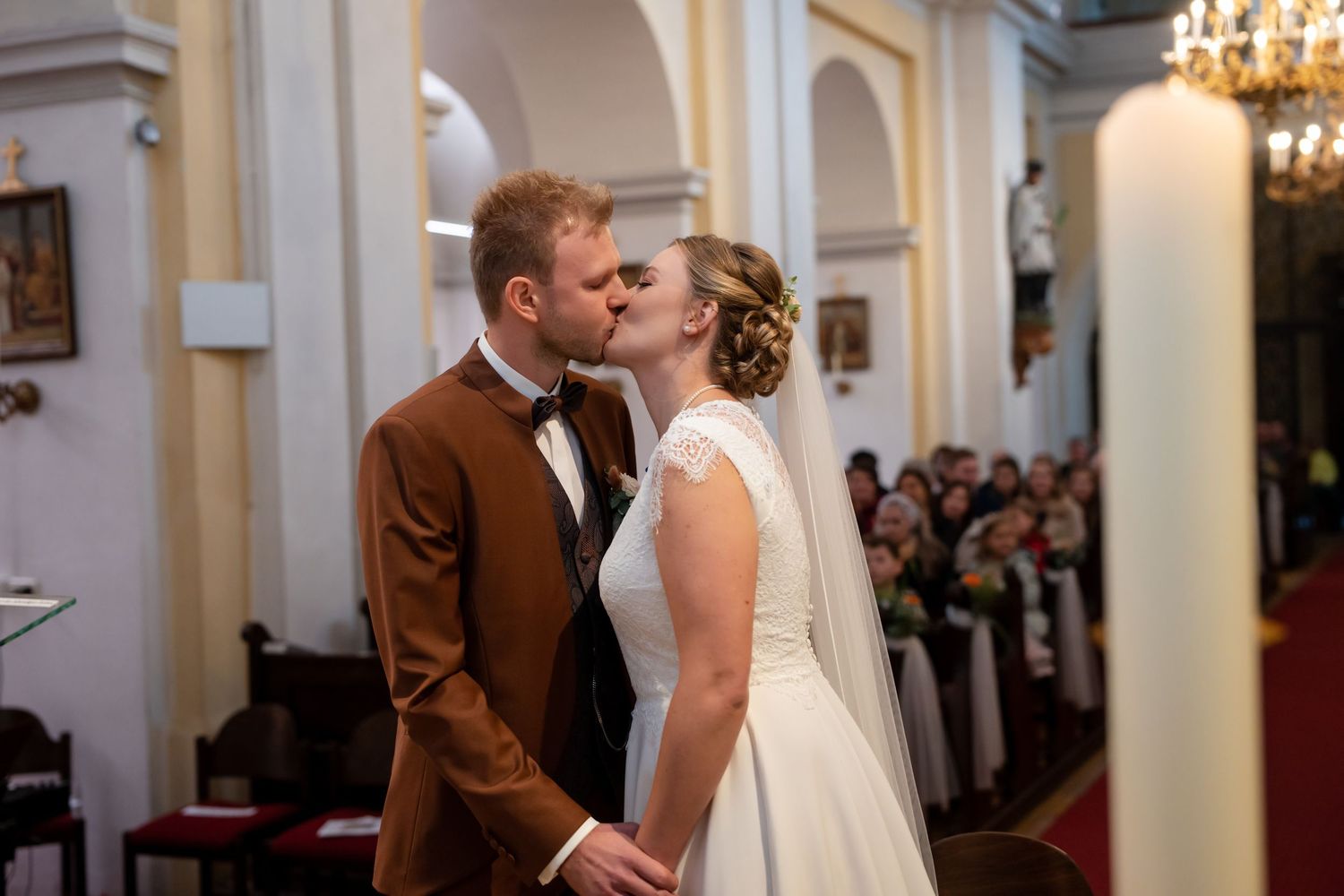 Romantic wedding ceremony moment inside an elegant church with chandeliers and arched architecture.