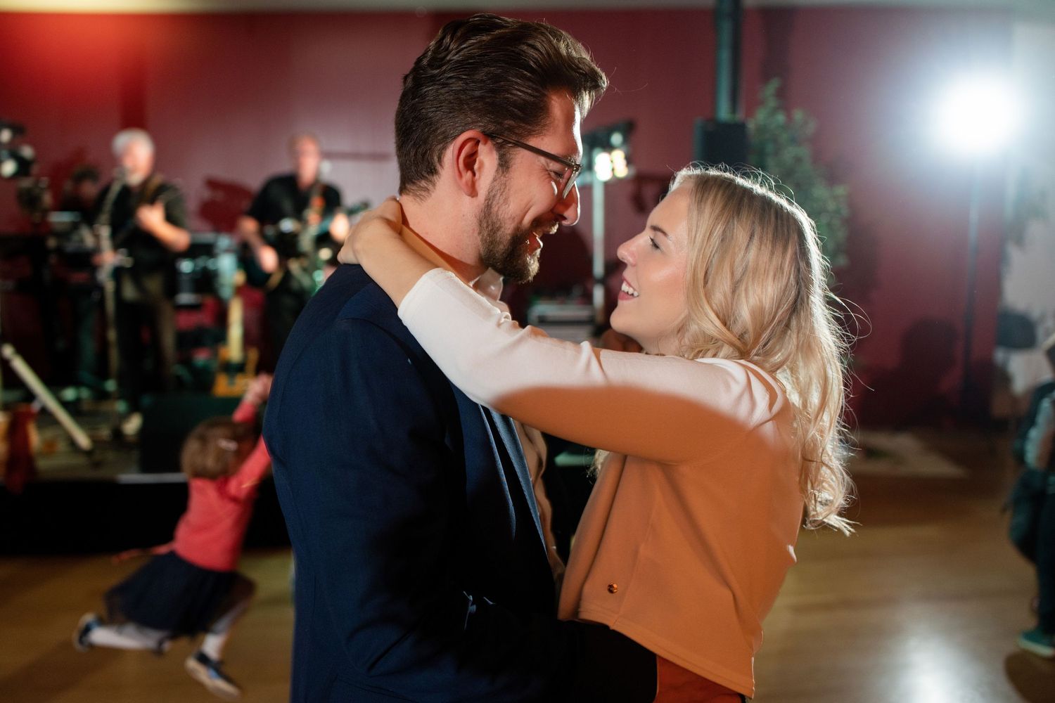 Couple dancing together in a venue with red walls and stage lighting.