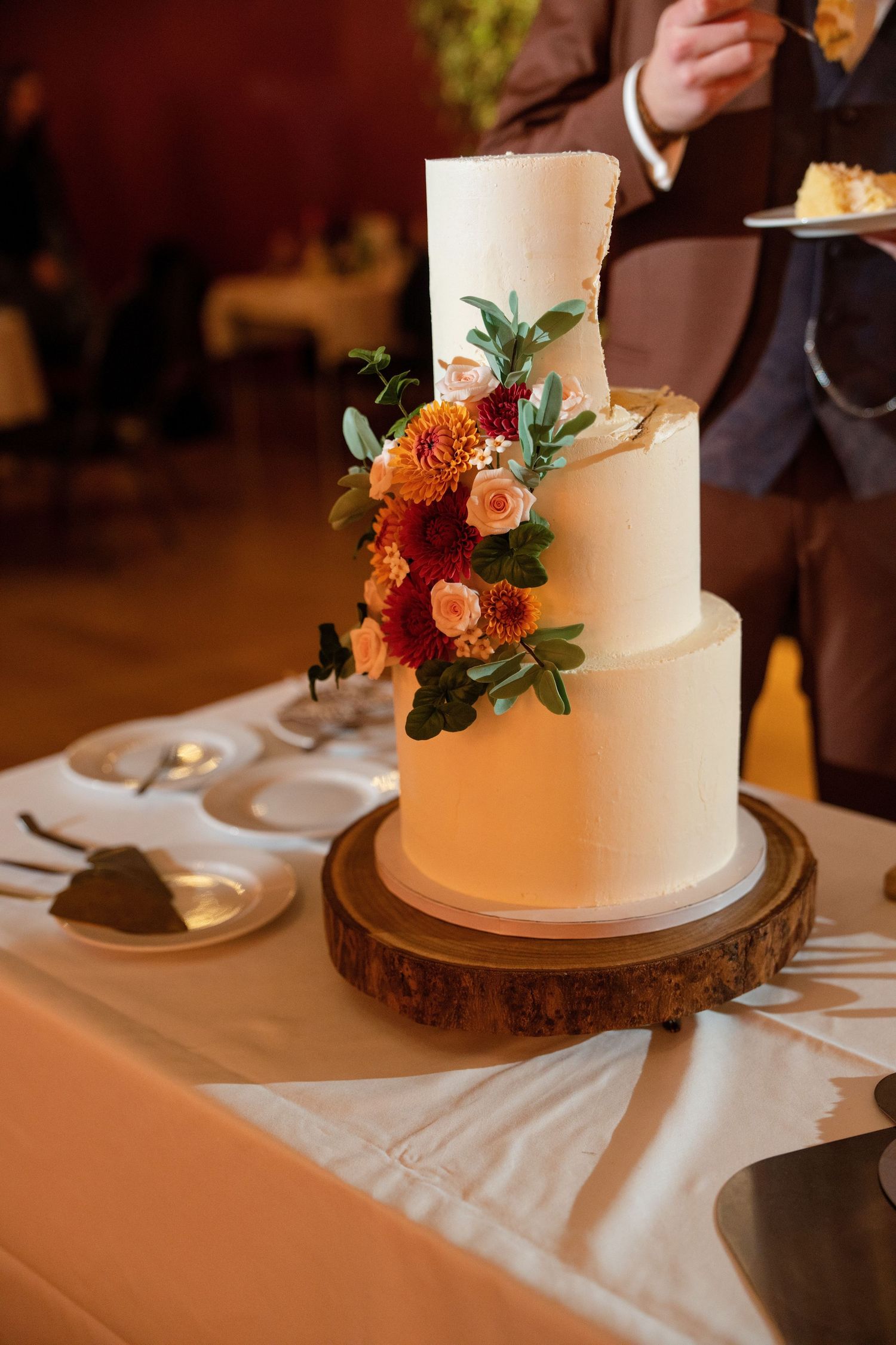 A three-tiered white wedding cake decorated with burgundy and pink flowers on a wooden stand.