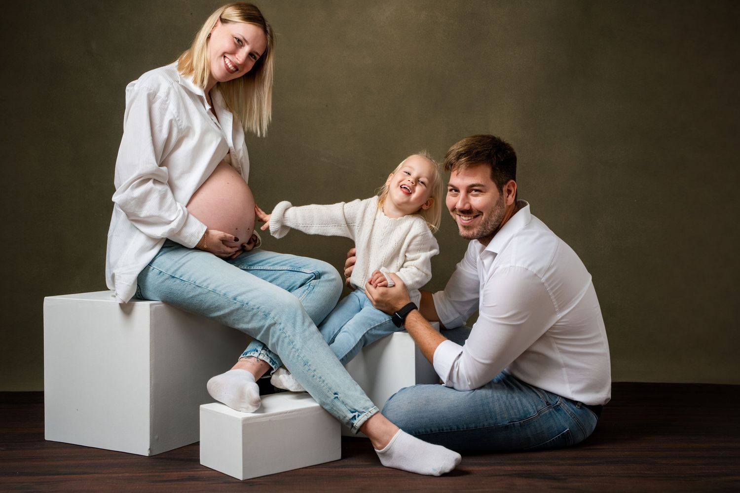 A couple shares playful moments while sitting and lounging on white geometric blocks against a dark wall.