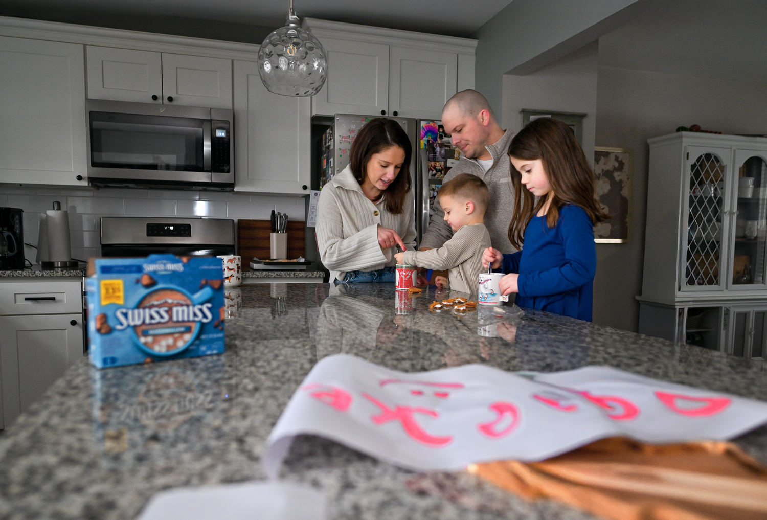 Family gathering in kitchen with pendant lights and granite countertops.