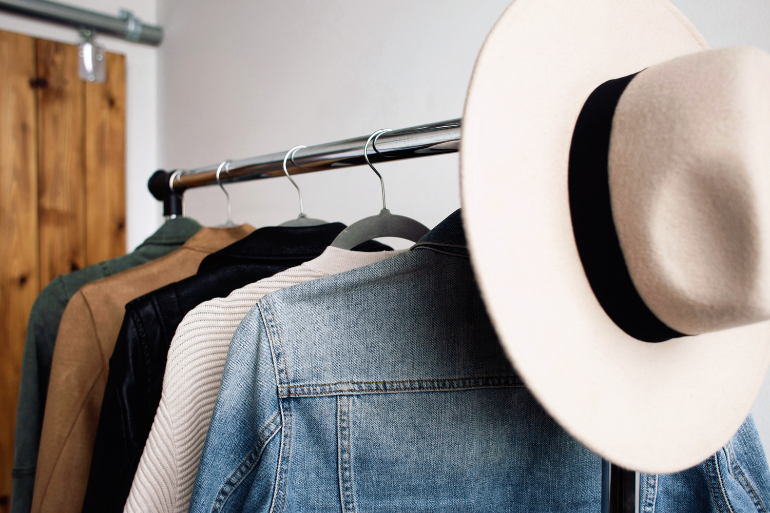 A row of white straw hats hanging on a wall mounted rack next to denim clothing in a retail store.